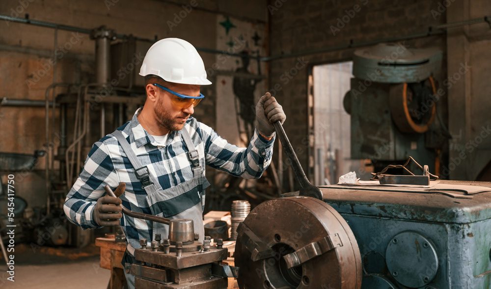 Focused on work with factory machine. Worker in uniform is indoors Focused on work with factory machine. Worker in uniform is indoors