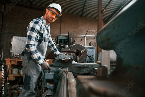 Focused on work with factory machine. Worker in uniform is indoors