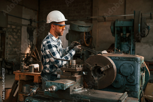 In defensive glasses and hard hat. Factory male worker in uniform is indoors