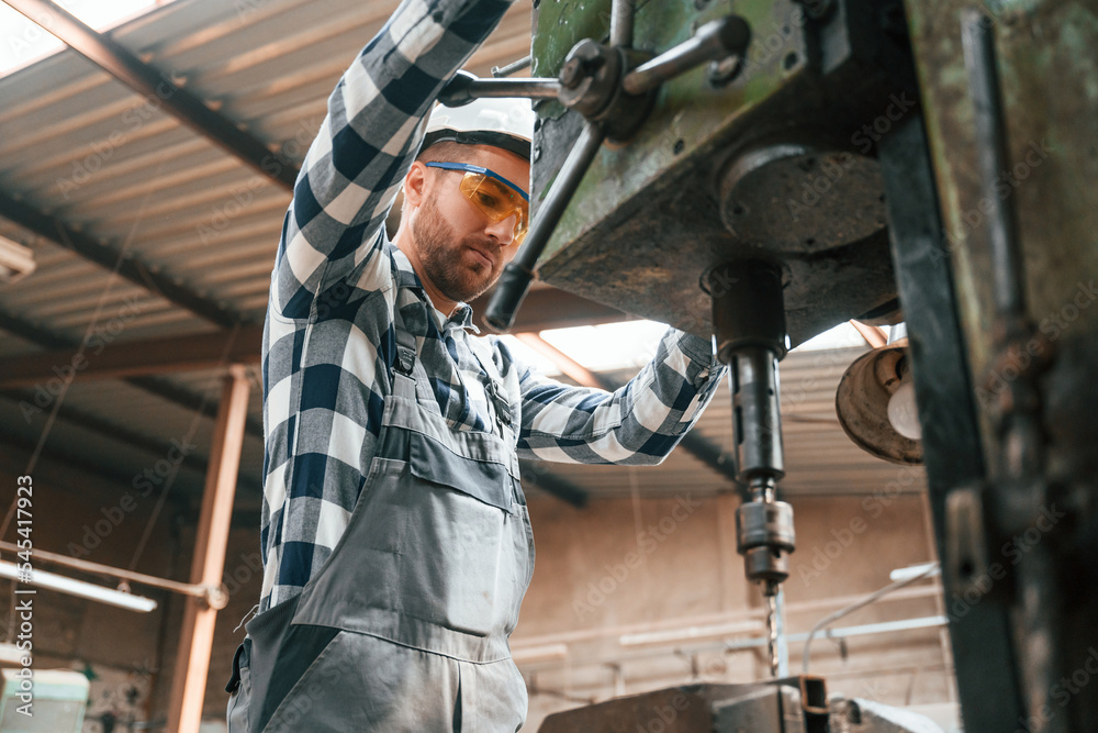 Factory male worker in uniform is indoors. Operating the drill machine