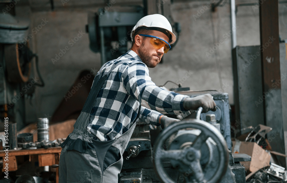 Manipulating the industry machine. Factory male worker in uniform is indoors Manipulating the industry machine. Factory male worker in uniform is indoors