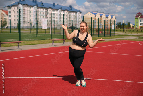 A young beautiful plus-size girl is enjoying success in losing weight standing on a sports field outside on a hot summer day. Cheerful mischievous woman © Maryna