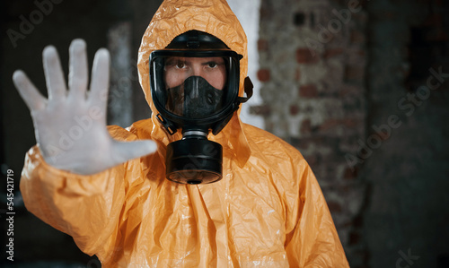 Stop sign by hand. Man dressed in chemical protection suit in the ruins of the post apocalyptic building