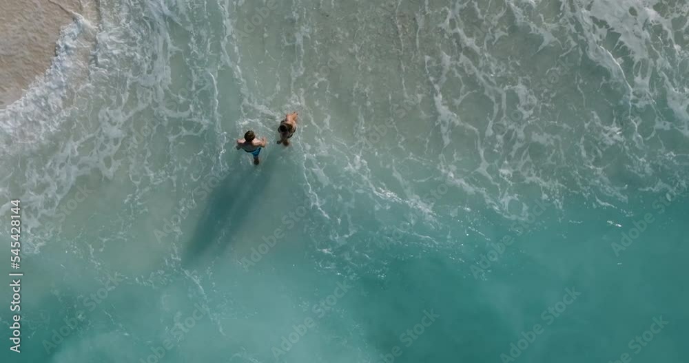 Straight down aerial view of a romantic couple walking out the surf after swimming in a turquoise sea on a tropical island Straight down aerial view of a romantic couple walking out the surf after swimming in a turquoise sea on a tropical island