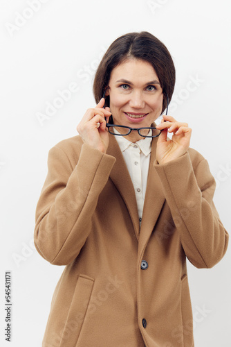 beautiful, attractive woman in a fashionable stylish coat puts on her glasses for vision while standing on a light background