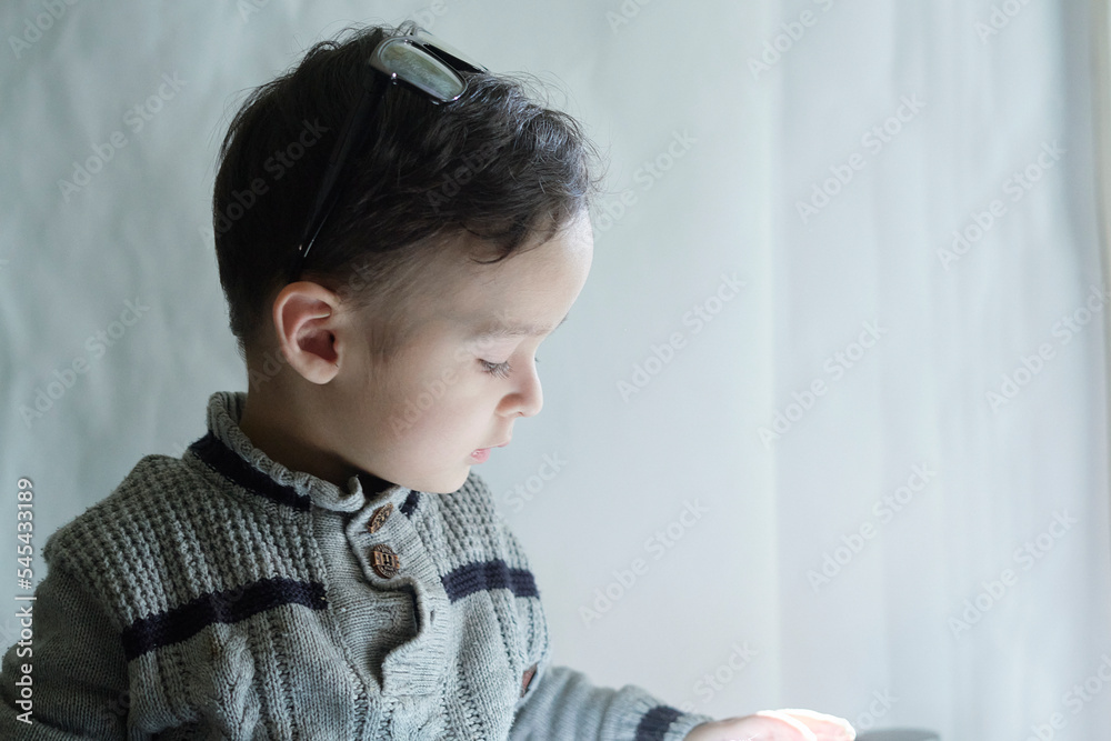 a little boy that is looking at something in his hand while he sits on the window sie and looks down a little boy that is looking at something in his hand while he sits on the window sie and looks down