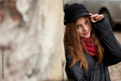 Girl in a black cap with a red scarf on a city street