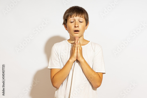 a teenager prays with his eyes closed. hard light, white background.