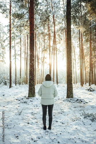 Vertical shot of the woman in a white puffer jacket against the background of snow-covered trees.