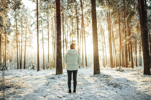 Woman in a white puffer jacket against the background of snow-covered trees on a sunny day.