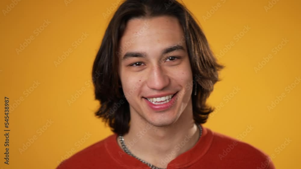Closeup slow motion portrait of smiling Latino Hispanic gender fluid non-binary, young man 20s wearing orange shirt isolated on yellow color background in studio. Sincere emotions lifestyle concept. Closeup slow motion portrait of smiling Latino Hispanic gender fluid non-binary, young man 20s wearing orange shirt isolated on yellow color background in studio. Sincere emotions lifestyle concept.