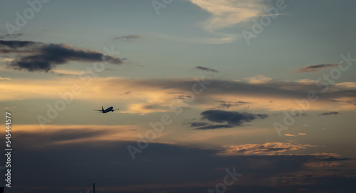 Jet airplane take off in sunset. Dark silhouette of a plane is gaining altitude. Against a background of yellow sky