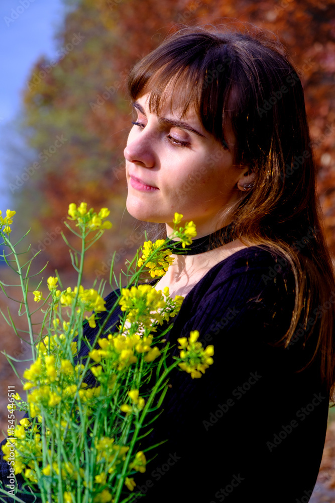 Naklejka premium Beautiful young girl in a black dress with green wildflowers on the photo of the autumn forest