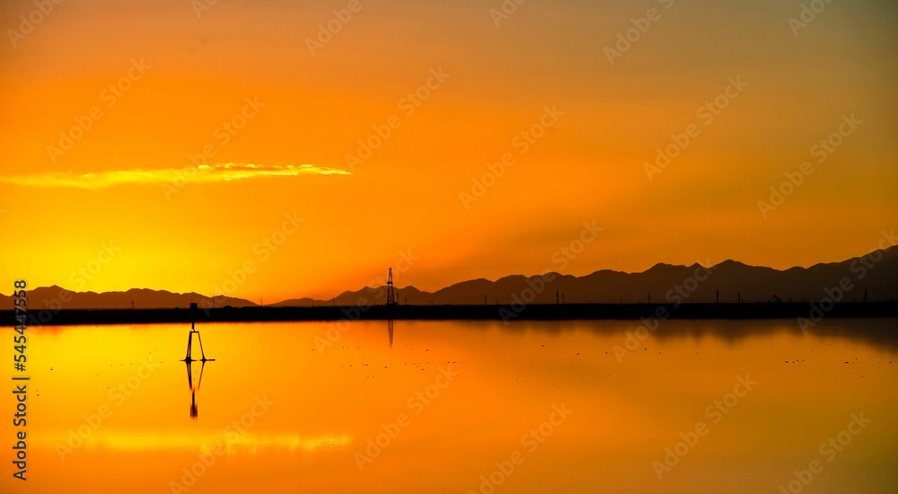 Breathtaking orange and yellow sunset sky and its reflection in the lake with mountain silhouettes