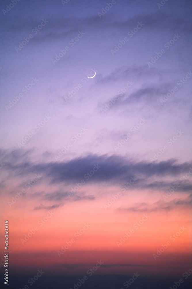 Pink and purple tones during twilight, with a small slice of moon in the sky