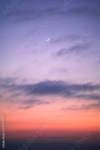 Pink and purple tones during twilight, with a small slice of moon in the sky