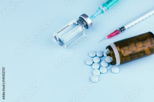 Closeup of pills and a container with a syringe on blue background