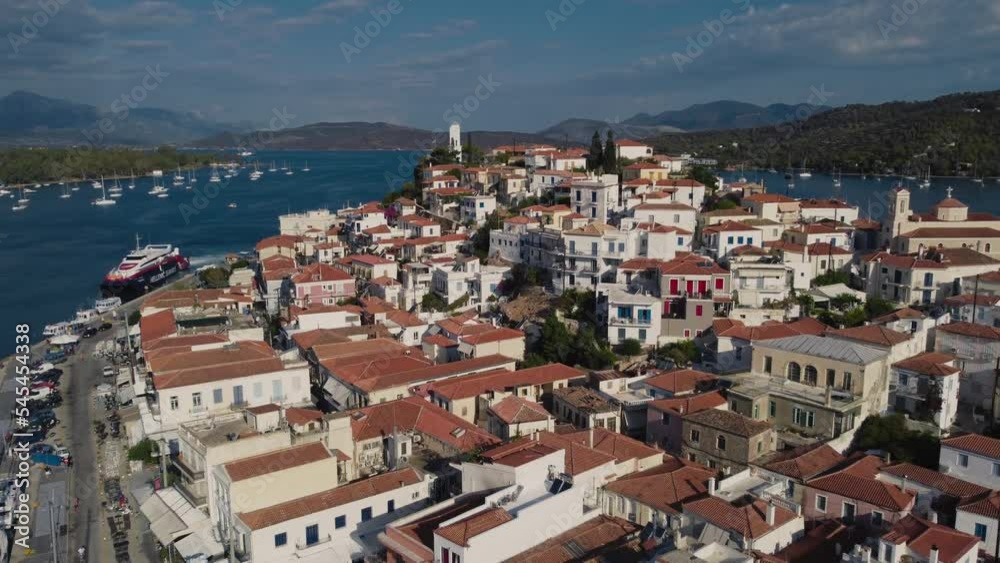 Drone shot of Poros with sunlit seascape and boats near, mountains, cloudy sky background Drone shot of Poros with sunlit seascape and boats near, mountains, cloudy sky background