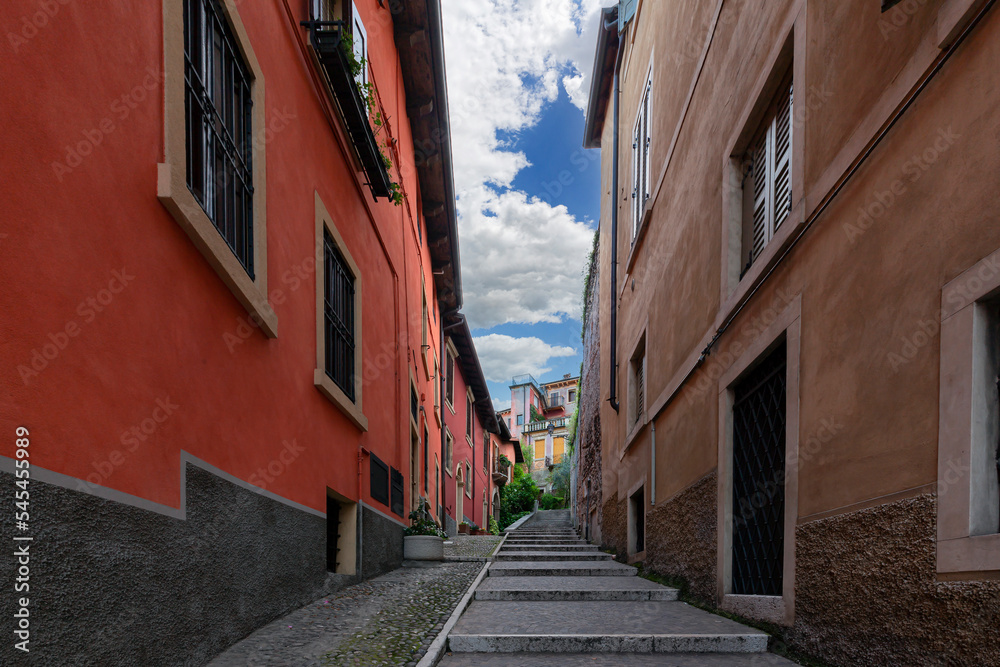 Narrow little street with stairs in Verona, Italy red and orange walls of buildings and wooden windows. City street with old architecture and green flowers.