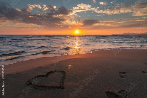 Scenic shot of a heart on an empty sandy beach at sunset