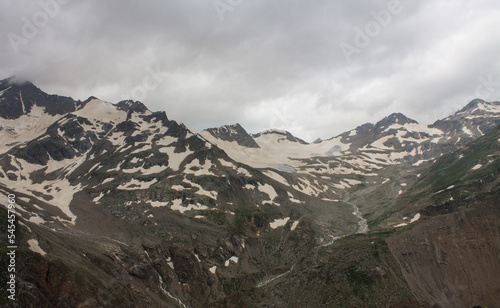 The high snow-capped peaks of the mountains in the Elbrus region in the North Caucasus and the cloudy sky with a blurred misty haze over the peaks and the space for copying