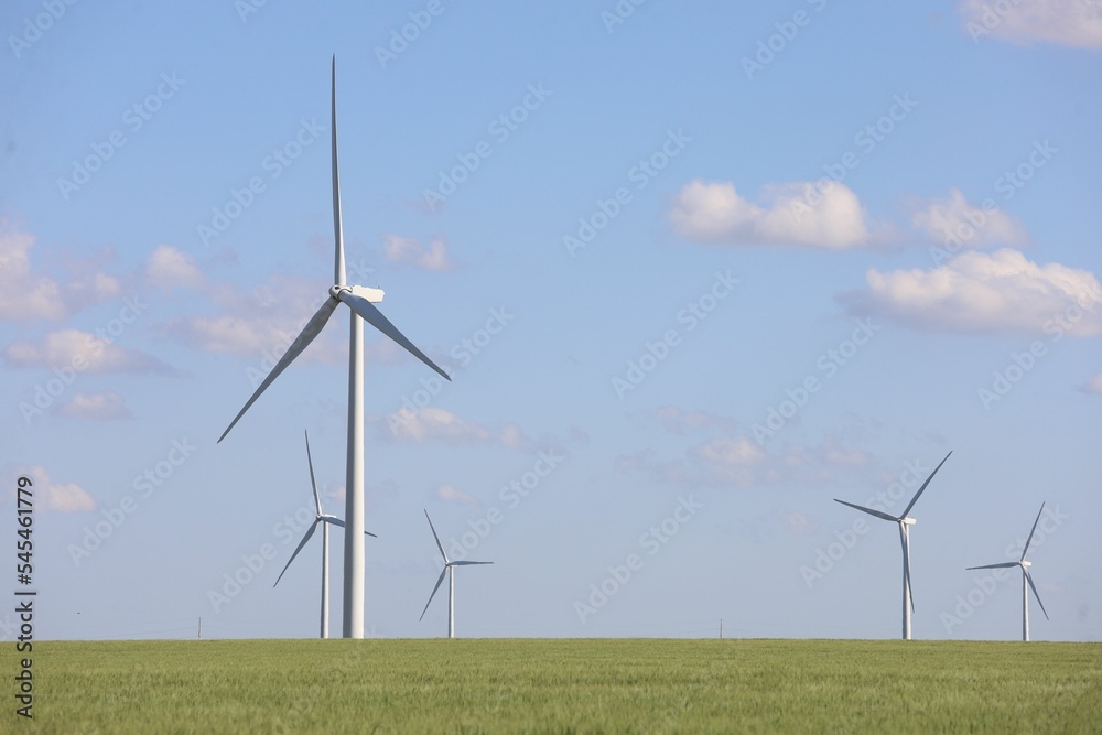 Landscape with wind generator turbines in a green field and a cloudy blue sky in the background Landscape with wind generator turbines in a green field and a cloudy blue sky in the background