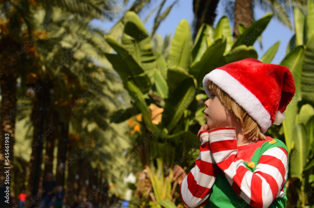 Cute boy in santa claus hat. Christmas at a tropical resort, family trip, children's emotions: surprise, joy, smile