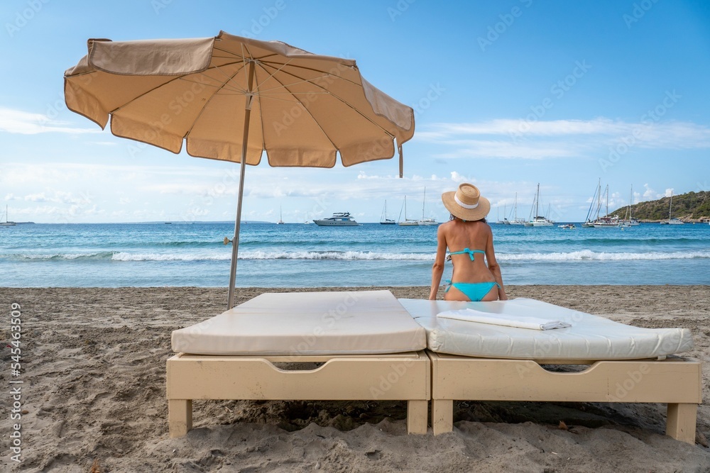 Attractive woman in a bikini looking at the sea sitting on a bed on the beach, Salines, Ibiza, Spain