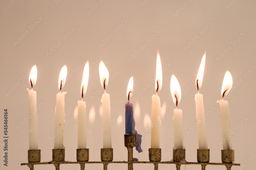 A full menorah on the last night of Hanukkah. Eight of the candles are white and the center one is blue. All nine candles are lit and reflecting in the background A full menorah on the last night of Hanukkah. Eight of the candles are white and the center one is blue. All nine candles are lit and reflecting in the background
