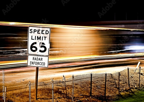Pole with a speed limit 65 sign on the background of light trails of cars in a long exposure shot photo