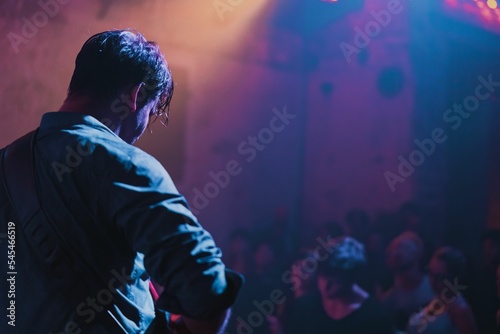 Backside view of a musician guy on the stage performing in front of the crowd