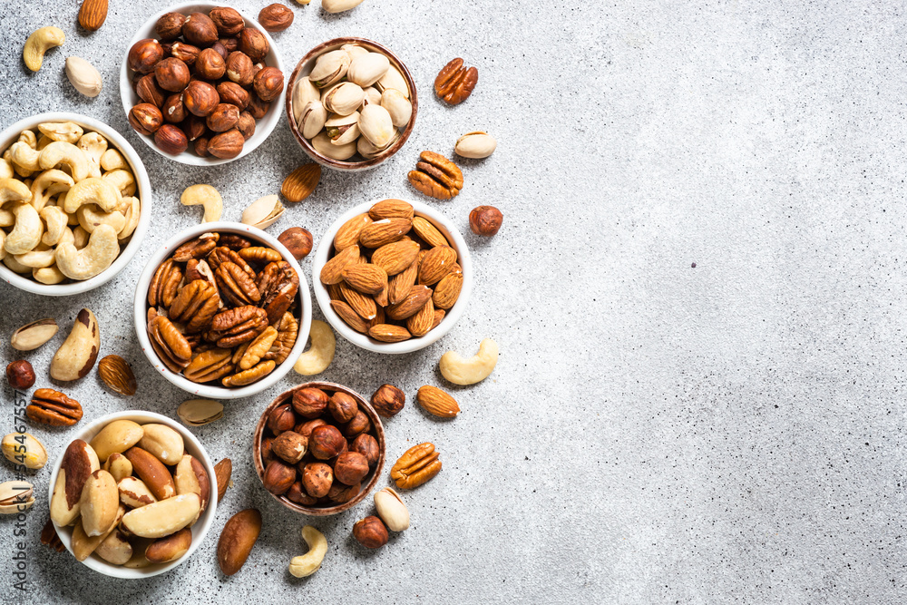 Assortment of nuts in bowls. Cashew, hazelnuts, pecan, almonds, brazilian nuts and pistachios at light table. Top view with copy space.