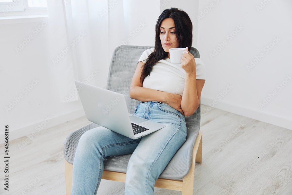 Woman relaxing at home sitting on a chair and watching a movie on her laptop with a cup of tea, smile autumnal mood