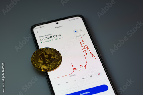 Bitcoin chart trends on Smartphone app with bitcoin gold coin on empty space. Cryptocurrency concept