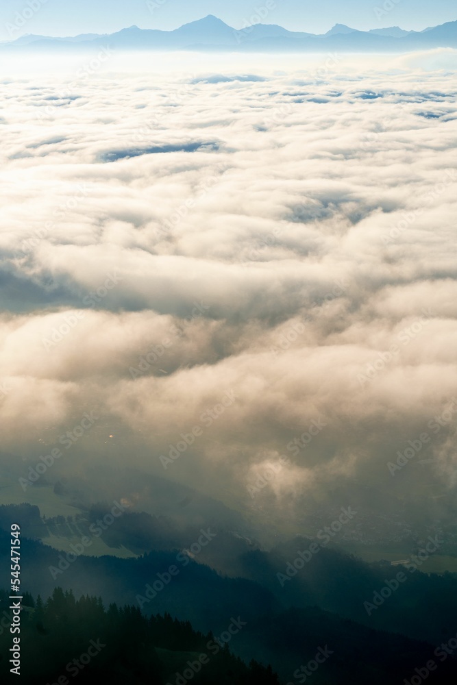 Vertical aerial shot of mesmerizing cumulative clouds over a foggy forest, mountains on the horizon