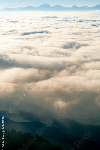 Fototapeta Naklejka Na Ścianę i Meble -  Vertical aerial shot of mesmerizing cumulative clouds over a foggy forest, mountains on the horizon