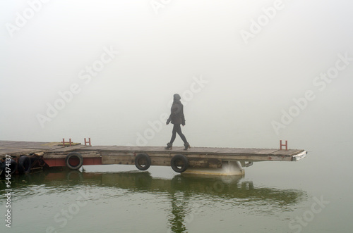 Young woman walking down the wooden dock in the mist on a cold autumn day