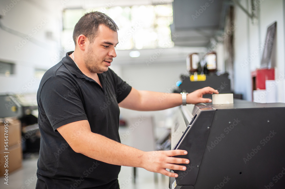 Fototapeta premium In the printing house, an experienced technician works on a UV printer. Production work. Check the print quality.