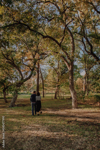 couple walking in park with tall trees