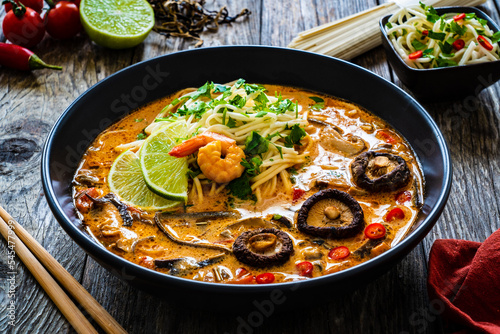 Tom Yum - Thai soup with prawn, shiitake mushrooms and noodles on wooden table
