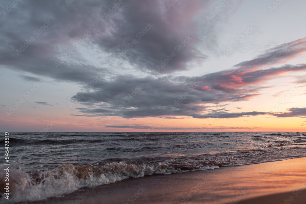 Orange sunset on the mediterranean sea, waves with golden sand. Pink clouds.