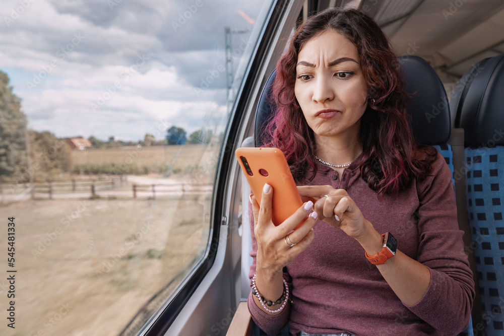 Annoyed girl unsuccessfully tries to catch a cellular signal or an unstable WiFi, holding her smartphone in her hands in train