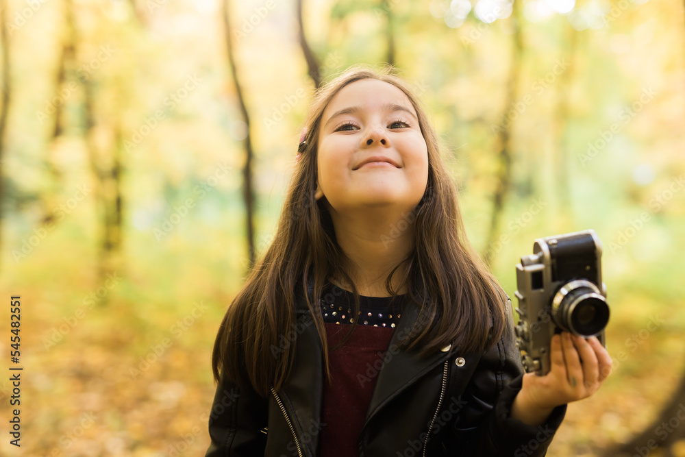 Child girl using an old-fashioned camera in autumn nature. Photographer, fall season and leisure concept.