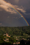 Beautiful rainbow over a medieval rural village with a castle upon a green hill at twilight. Italy, Piedmont.