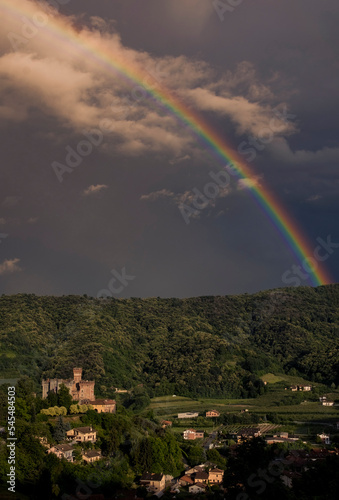 Obraz na płótnie Beautiful rainbow over a medieval rural village with a castle upon a green hill at twilight. Italy, Piedmont. w salonie