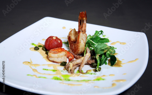 Grilled shrimps or prawns served with greens, garlic and white sauce on a white plate. Seafood. Side view