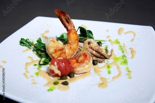 Grilled shrimps or prawns served with greens, garlic and white sauce on a white plate. Seafood. Side view