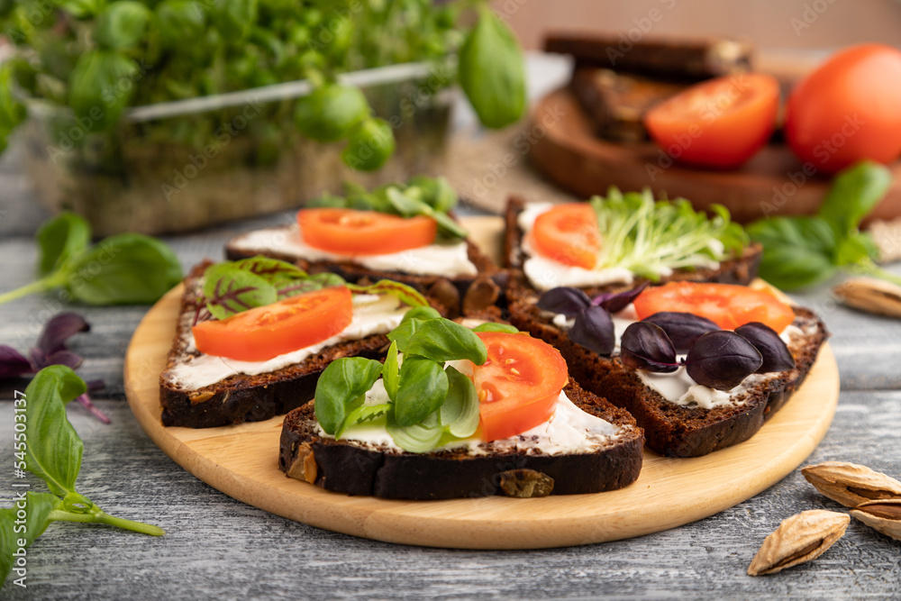 Grain rye bread sandwiches with cream cheese, tomatoes and basil microgreen on gray. side view, selective focus.