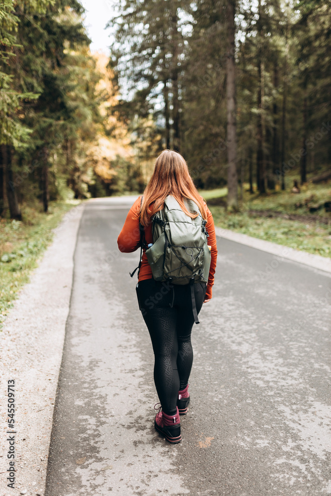 Solo tourist Woman hiking on footpath in autumn forest. Full body photo. Happy redhead person in active trekking clothes walking on nature backgraund. Travel and active lifestyle concept. Solo tourist Woman hiking on footpath in autumn forest. Full body photo. Happy redhead person in active trekking clothes walking on nature backgraund. Travel and active lifestyle concept.