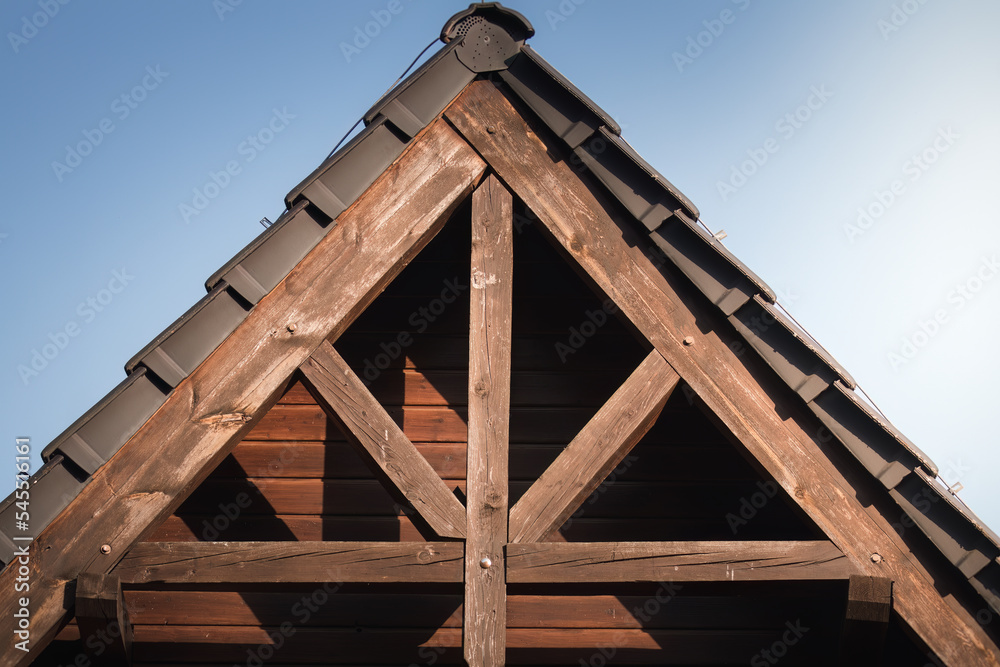 Roof truss in the setting sun. Wooden, thick beams, thick planks, brown structure supporting the roof. Roof with tiles. Roof truss in the setting sun. Wooden, thick beams, thick planks, brown structure supporting the roof. Roof with tiles.